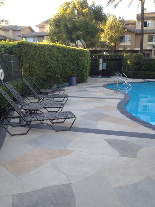 Example of concrete deck coatings that look like grey and tan flagstones around a swimming pool