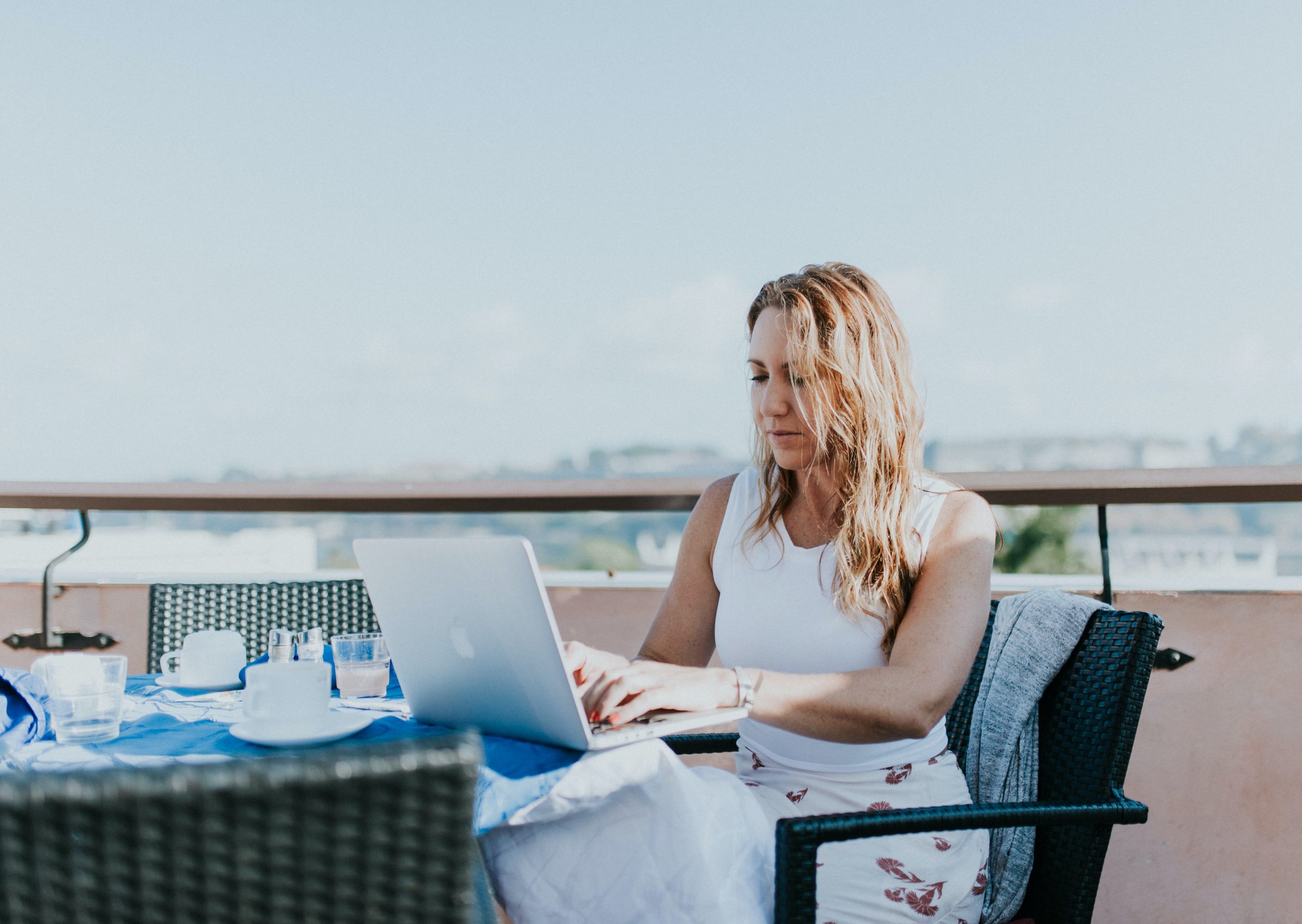 woman sitting in chair on roof deck using a laptop to check credentials of roofer for flat roof repairs