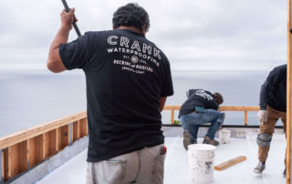 men rolling flat roof coatings to building by the ocean