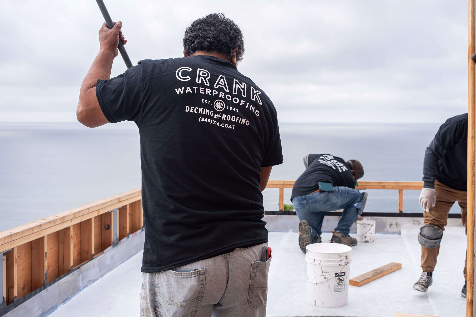 men rolling flat roofs coating to building by the ocean