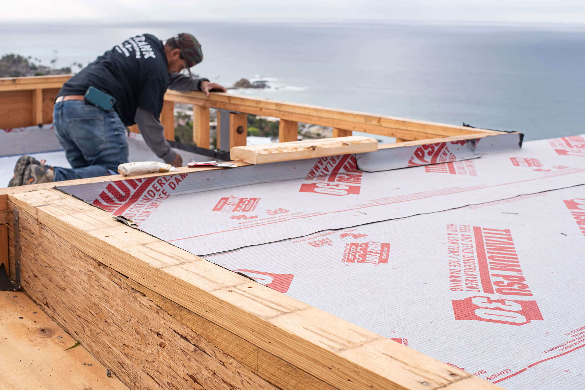 man working on orange county flat roofs with ocean in background