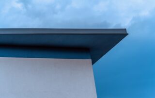grey house with flat roof coating against blue sky