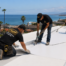Crank workers in black tee shirts installing single ply TPO to Orange County flat roof